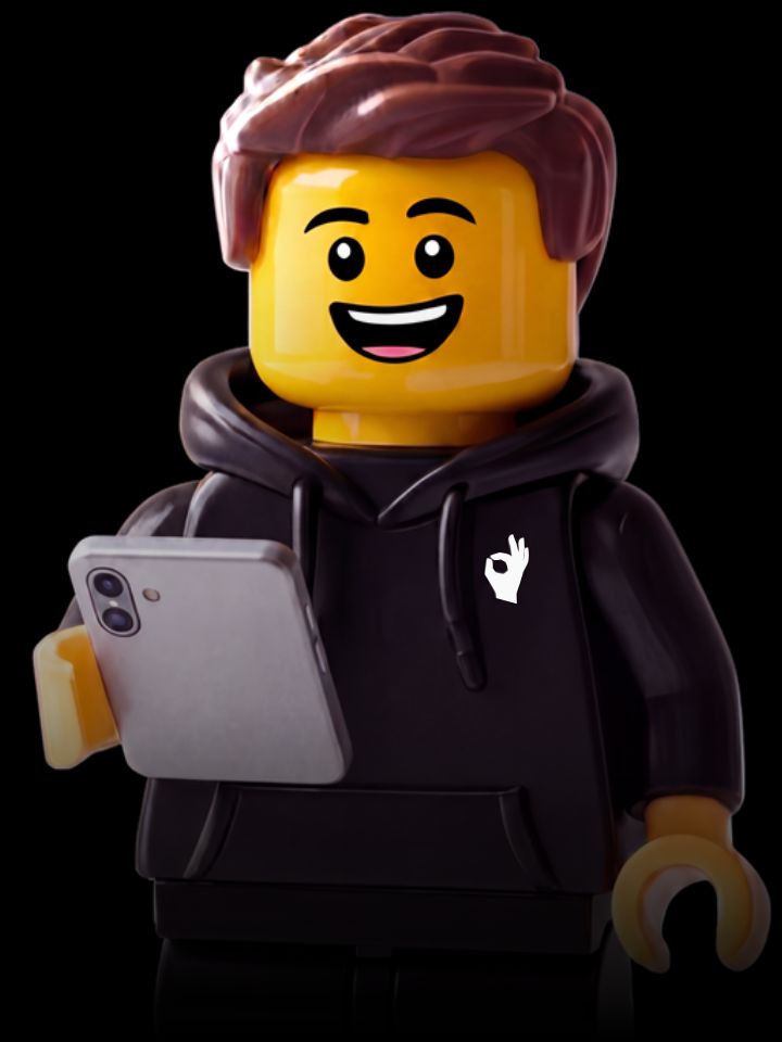 Smiling LEGO minifigure with brown hair wearing a white hoodie with a blue OK hand symbol, holding a silver smartphone.